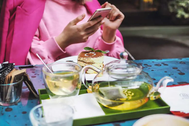 Women in pink, holding a phone at a table with brunch and tea